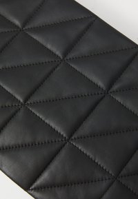 Materiale in pelle nera con un motivo a rombi, caratterizzato da cuciture prominenti e una superficie liscia.