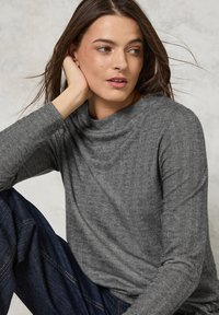 Grå herringbone-mönstrad långärmad topp med avslappnad passform, som har en vid halsringning och texturerad tyg, matchad med mörkblå jeans.