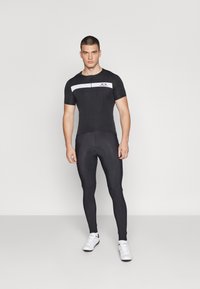 Schwarzer Fahrradanzug mit kurzen Ärmeln, Reißverschluss vorne und weißen horizontalen Streifen. Enganliegende Leggings in einfarbig Schwarz, glatte Textur und ohne Muster.