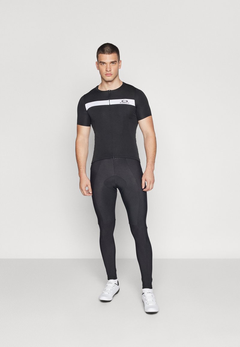 Schwarzer Fahrradanzug mit kurzen Ärmeln, Reißverschluss vorne und weißen horizontalen Streifen. Enganliegende Leggings in einfarbig Schwarz, glatte Textur und ohne Muster.
