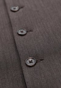 Gros plan d’un tissu chevron marron avec des boutons à quatre trous marron foncé cousus en ligne verticale.
