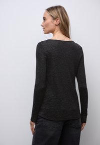 Zwarte lange mouwen top met een subtiele glans, voorzien van een ronde halslijn en een gladde textuur. Model draagt het met donkergrijze broek.