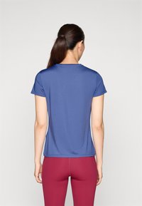Blauwe sporttop met korte mouwen en een ronde hals, gecombineerd met fitted bordeauxrode legging. Soepele stof met een licht rekbare textuur.