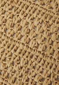 Tappeto intrecciato realizzato con fibre naturali di colore beige. Presenta un design testurizzato, intrecciato, con un motivo aperto e una finitura morbida.