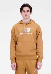 Sudadera color mostaza con bolsillo canguro, puños y dobladillo acanalados, que presenta el logo blanco de "new balance" en el pecho. Tejido suave, corte holgado.
