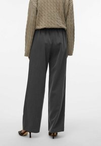 Szerokie szare spodnie o fakturowanym, miękkim materiale i elastycznym pasku, zestawione z jasnobeżowym swetrem w warkocze i obcasami.