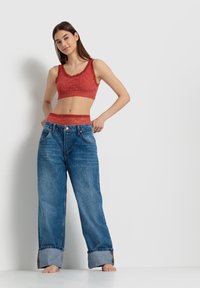 Red lace bralette with scalloped edges paired with loose-light blue denim jeans, featuring a cuffed hem and two front pockets.