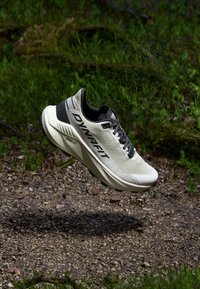 Ελαφρύ αθλητικό παπούτσι τρεξίματος σε μπεζ και μαύρο. Διαθέτει υφαντό επάνω μέρος, μαξιλαρωμένο κολάρο και κορδόνια. Η σόλα σχεδιασμένη για απορρόφηση κραδασμών και υποστήριξη.