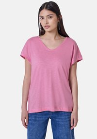Růžové tričko s krátkým rukávem a výstřihem do V, vyrobené z lehké, měkké tkaniny. Volný střih s hladkou strukturou. V kombinaci s modrými denimovými džíny.
