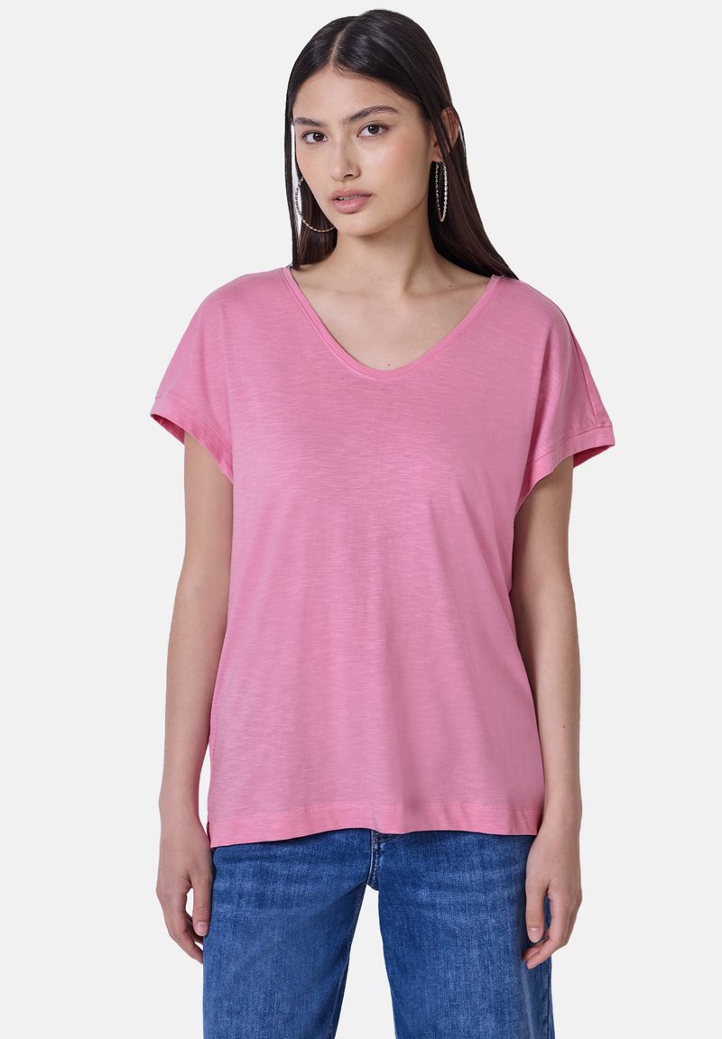 Růžové tričko s krátkým rukávem a výstřihem do V, vyrobené z lehké, měkké tkaniny. Volný střih s hladkou strukturou. V kombinaci s modrými denimovými džíny.