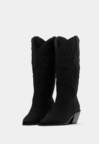 Ζευγάρι μαύρα δυτικά μπότες μεσαίου ύψους μέχρι τη μέση της γάμπας,  με μυτερές μύτες, τακούνια πλατφόρμα και διακοσμητικό ραφές σε λείο δέρμα.