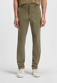 Olijfgroen op maat gemaakte broek met een subtiele textuurpatroon, voorzien van een standaard tailleband en voorzakken, gecombineerd met witte sneakers.