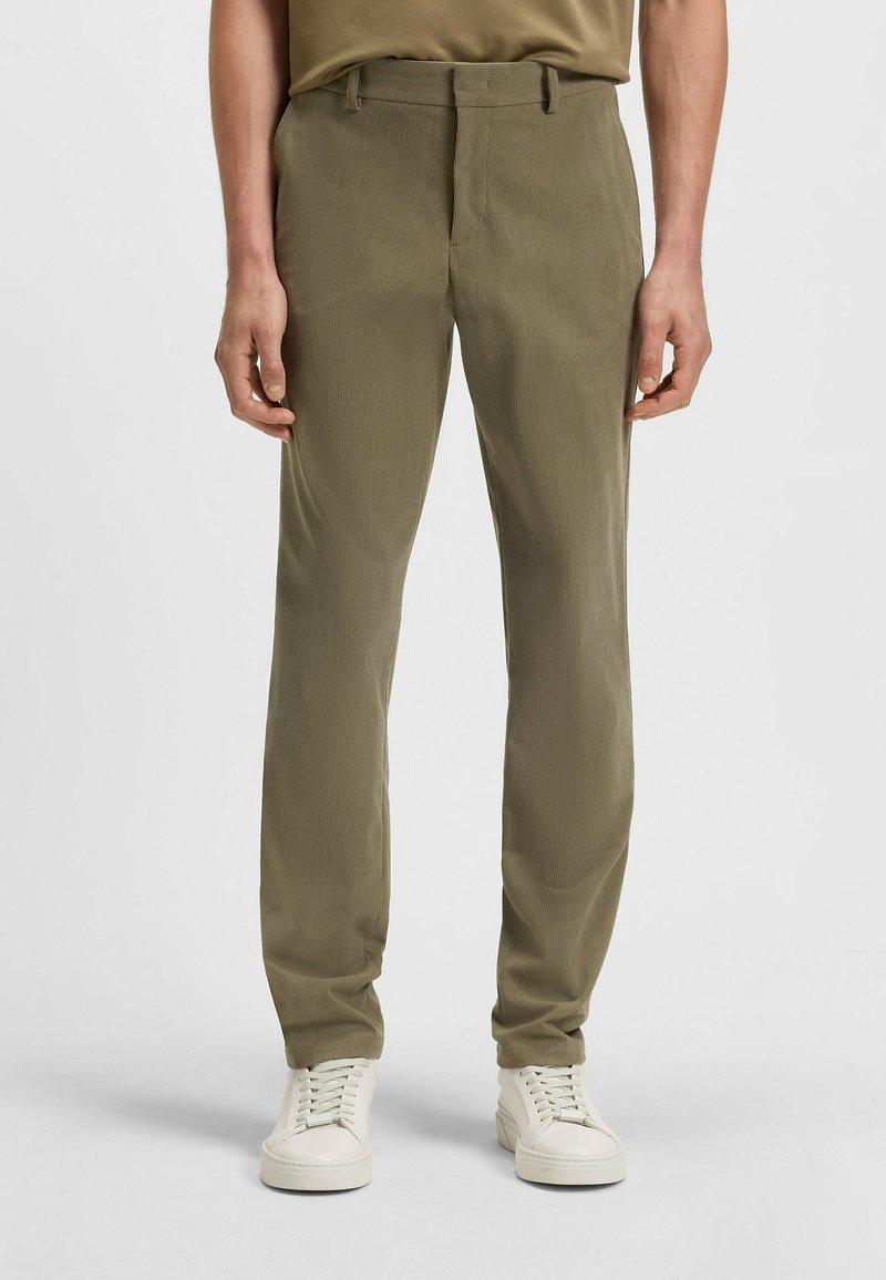 Olijfgroen op maat gemaakte broek met een subtiele textuurpatroon, voorzien van een standaard tailleband en voorzakken, gecombineerd met witte sneakers.