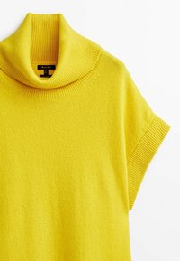 Keltainen korkeakauluksinen lyhythihainen neulepaita, joka on valmistettu pehmeästä neulekankaasta. Siinä on korkea, ribattu kaulus ja sileä pinta.