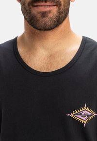 Top de tirantes negro con escote redondo y un diseño gráfico que presenta un ojo y un destello de sol en rosa y amarillo en el lado izquierdo del pecho.