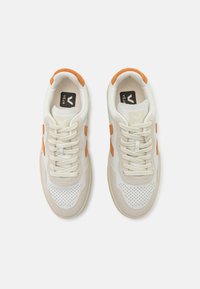 Scarpe da ginnastica bianche e beige con accenti arancioni, dotate di una punta perforata, lacci piatti e suole imbottite. Elementi in suede texturizzato.