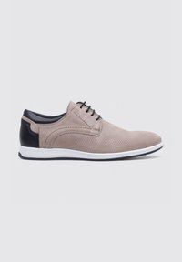 Zapato de cuero perforado beige con acentos de cuero negro, punta redonda, suela blanca y seis pares de ojetes para los cordones.
