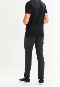 Svart bomullströja med korta ärmar i kombination med mörkgrå skinny jeans. Svarta sneakers med vita sulor fulländar outfiten.