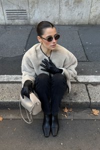 Mākslīgās kažokādas beigu krāsas mētelis, melni ādas cimdi, melni džinsi un kvadrātveida melnas potīšu zābaki. Tur rokās gaiši beigu krāsas somu.