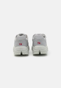 Gray sneakers with a textured upper, padded collar, and contrasting red numbers (19, 74) on the heel. Vibram branding on the sole.