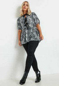 Top de estampado de serpiente en blanco y negro con mangas abullonadas y detalle de lazo en el frente, combinado con jeans ajustados negros y botas de tobillo brillantes.