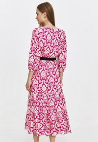 Sukienka w kwiatowy wzór z rękawami o długości trzech ćwiartek, czarnym paskiem w talii oraz rozkloszowanym, warstwowym dołem w kolorach różowym i kremowym.