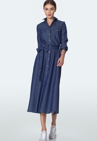 Sukienka koszulowa z denimu z długimi rękawami, zapinana na guziki z przodu, z dwiema kieszeniami na piersi i odpinanym paskiem. Posiada zwiewny spódnicę midi. Kolor: ciemnoniebieski.