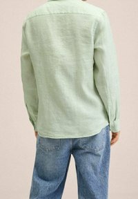 Chemise verte claire à manches longues en tissu texturé, dotée d'un col, de poignets à boutons, et d'une coupe décontractée, associée à un jean en denim bleu.