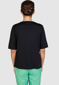 Black short-sleeve T-shirt with a round neckline, made of smooth fabric, worn with green pants, showing a simple and relaxed cut.