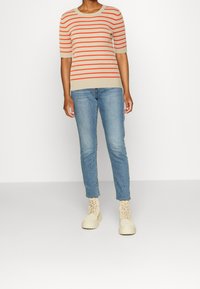 Beiger und rot gestreifter, kurzärmeliger, gerippter Pullover kombiniert mit hellblauen, eng anliegenden Jeans und cremefarbenen Schnürstiefeln.