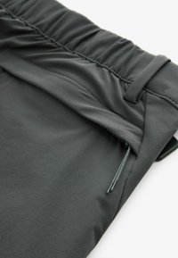 Gros plan sur un pantalon gris foncé avec une taille élastique, une poche latérale zippée et un cordon de serrage pour une fermeture sécurisée.
