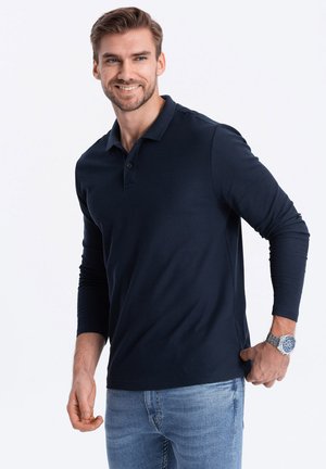 Polo a maniche lunghe blu navy con colletto, apertura a tre bottoni e texture liscia, abbinato a jeans azzurri chiari.