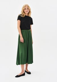 Czarna, krótko rękawowa koszulka połączona z długą, plisowaną, zieloną spódnicą. Całość uzupełniają czarne płaskie buty.
