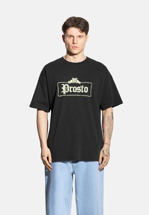 Czarny bawełniany t-shirt o luźnym kroju, z wyraźnym białym haftowanym logo "Prosto" z przodu. Krój z okrągłym dekoltem.