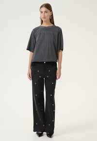 Grå bomuldsbluse med korte ærmer, parret med sorte vide bukser med metalknapper. Begge dele har et afslappet design.