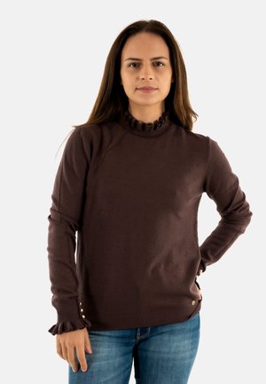 Suéter marrón de punto con puntos, alto cuello con volantes, mangas largas y puños con volantes. Presenta pequeños botones en el dobladillo. Combinado con jeans azul.