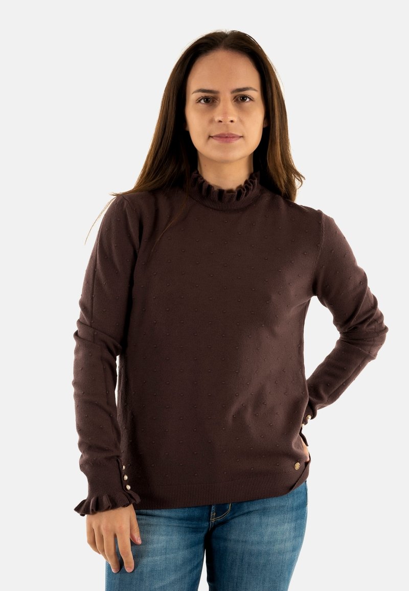 Maglione marrone lavorato a maglia con pois, colletto alto a ruches, maniche lunghe e polsini arricciati. Presenta piccoli bottoni all'orlo. Abbinato a jeans blu.