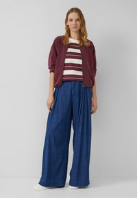 Bordeaux kleurige bomberjack over een wit en bordeaux gestreept shirt, gecombineerd met losse blauwe denim broek en witte sneakers. Eenvoudige, casual outfit.