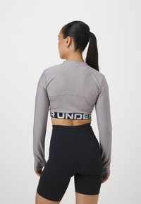 Grå langermet crop top med ribbet tekstur og svart "UNDER"-bånd; kombinert med høytlivede svarte shorts.