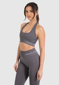 Sujetador deportivo gris y leggings de cintura alta hechos de tela elástica. Presenta un diseño recortado y el logo blanco "SMILOD" en la cinturilla.