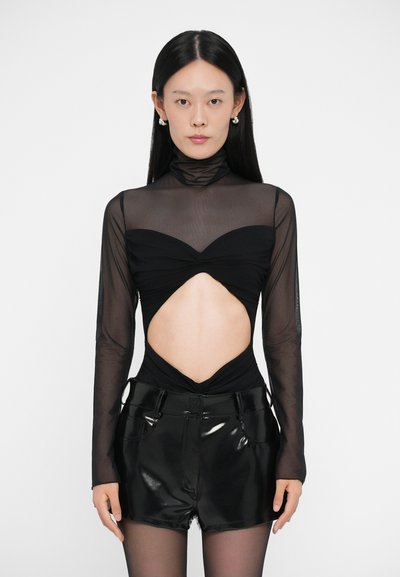 Top nero a maniche lunghe in rete trasparente con collo alto e design con ritagli, abbinato a pantaloni corti neri lucidi con tasche.