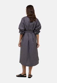 Robe longue rayée en tissu foncé avec des manches bouffantes, taille cintrée et ourlet au niveau du mollet. Portée avec des sandales plates à lanières.