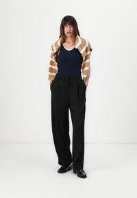 Navy tank top under a tan and white striped knit sweater, paired with high-waisted black trousers and black shoes. Smooth, relaxed fit.