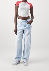 Vit crop top med röda ärmar, matchat med ljusblå, löst sittande jeans. Outfiten fullbordas av vita sneakers med färgade accenter.