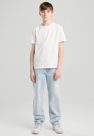 Weißes Baumwoll-T-Shirt kombiniert mit hellblauen Jeans. Die Jeans haben eine lockere Passform und eine ausgebleichte Textur. Weiße Sneakers runden das Outfit ab.