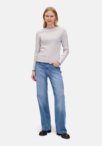 Gestreiftes Langarmhemd mit gewelltem Saum, kombiniert mit hellblauen weit geschnittenen Jeans und schwarzen Plateauschuhen.