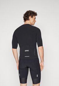 Maillot de cyclisme noir à manches courtes avec une poche zippée dans le dos, coupe slim, tissu texturé et logo POC dans le dos. Associé à un short noir.