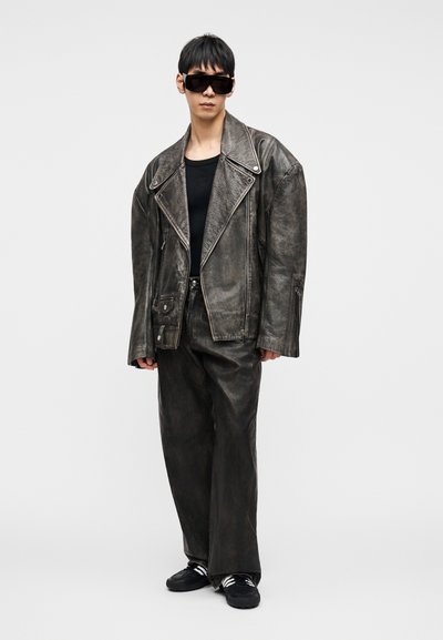 Ülerahvastatud tume nahkjakk tekstuurse viimistlusega, sobitatud lahtiste nahkpükstega ja mustade tossudega. Aksessuaaride hulka kuuluvad suured mustad päikeseprillid.