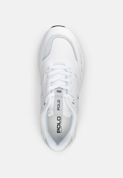 Zapatilla deportiva blanca con parte superior de malla, cierre de cordones y cuello acolchado. Presenta acentos grises y un logo en la lengüeta. Diseño de punta redondeada.