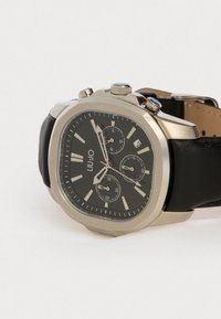 Μαύρο ρολόι με δερμάτινο λουράκι και οκταγωνίο ασημένιο καπάκι. Μαύρος δίσκος με ασημένιους δείκτες και τρεις υποδείκτες. Διαθέτει κουμπιά και παράθυρο ημερομηνίας.